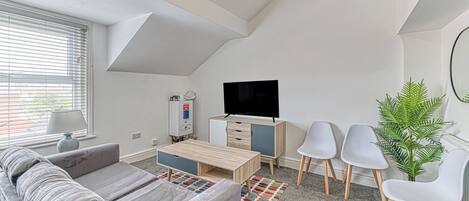 A modern, compact living space with a sofa, a TV, a small cabinet, and a potted plant.