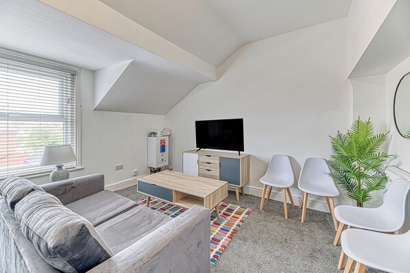 A modern, compact living space with a sofa, a TV, a small cabinet, and a potted plant. - Double Bed Apts Fairhaven View by Guestz (Lytham St. Anne's)