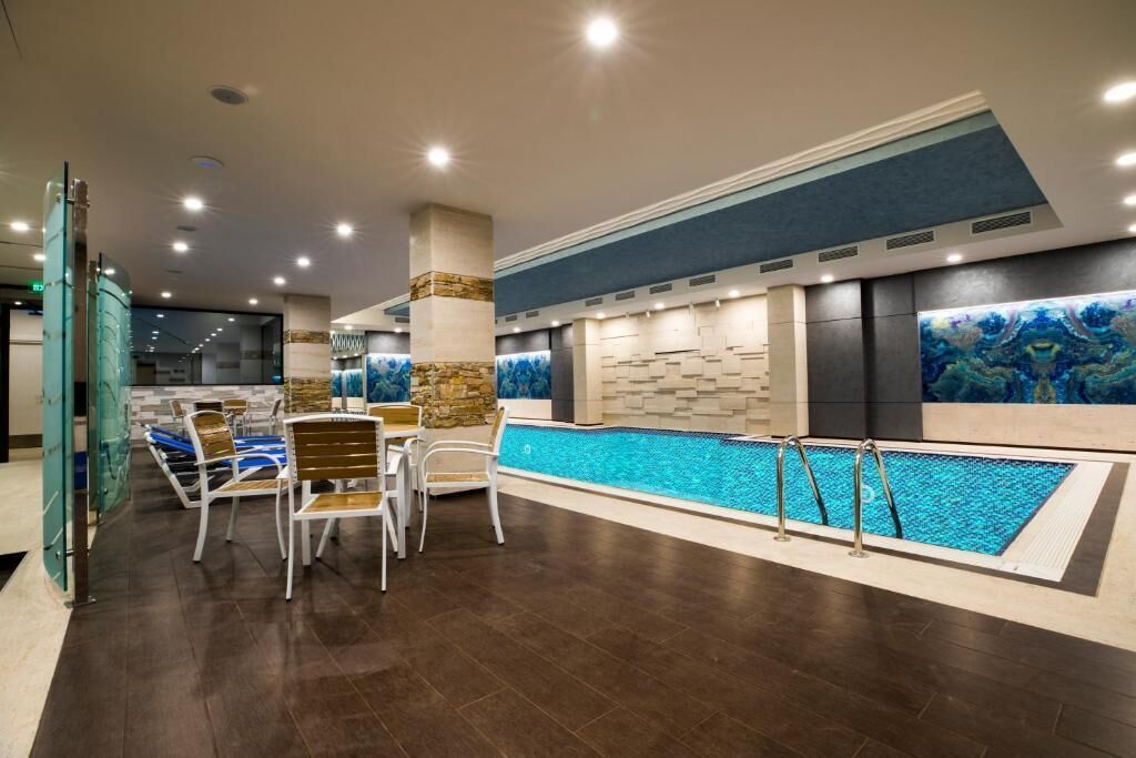 Un área de piscina interior con una pileta larga, sillas de descanso y una pared de piedra con un cuadro abstracto azul.