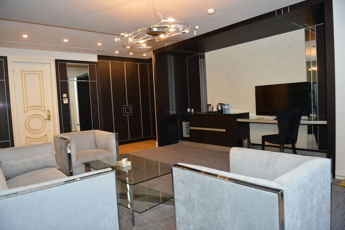 A modern living room with a glass coffee table, two armchairs, a sofa, a flat-screen TV, and a dark wood accent wall.