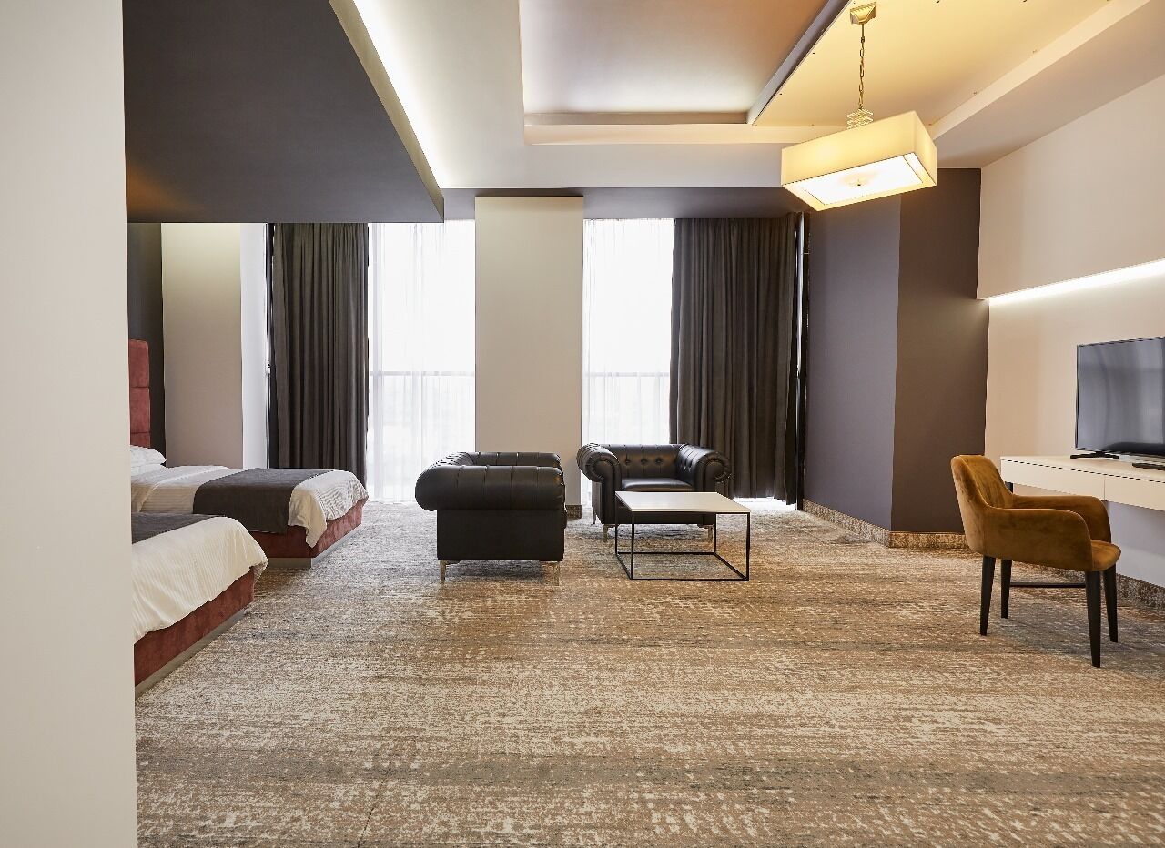 A hotel room with a large bed, a sofa, a desk with a chair, and a television.