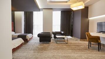 A hotel room with a large bed, a sofa, a desk with a chair, and a television.
