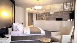 A modern hotel room with a bed, a chair, a small round table, and a decorative wall panel.