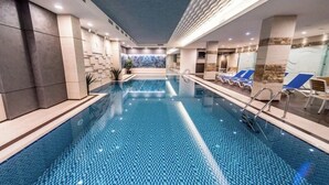 An indoor swimming pool with clear water, surrounded by lounge chairs and a tiled wall with a geometric pattern.