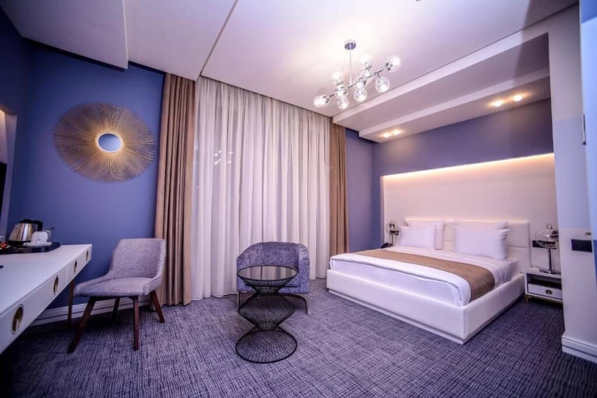 A modern hotel room with a large bed, a desk, a chair, and a small table.