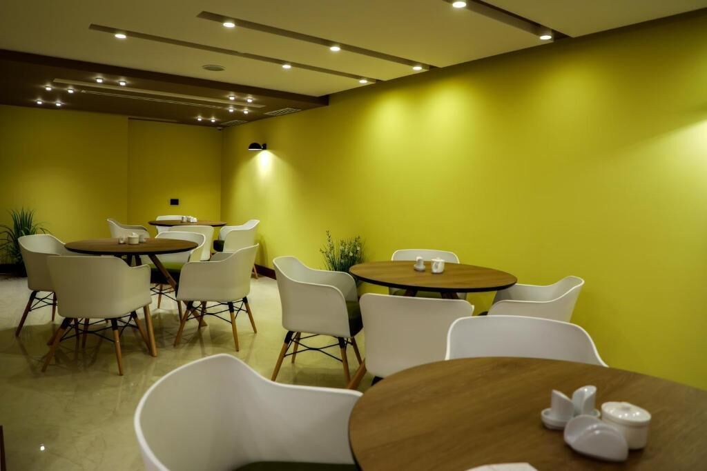 A modern dining area with round tables and white chairs, yellow walls, and recessed ceiling lighting.