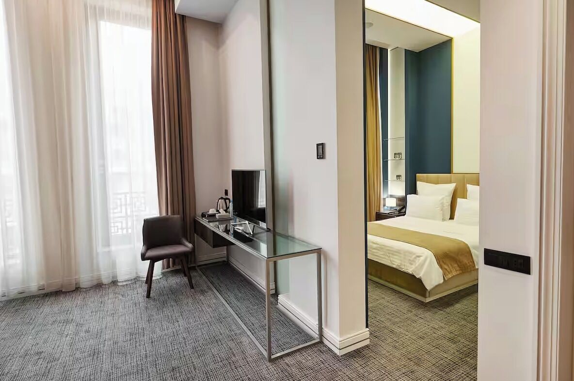 Een hotelkamer met een bed, een bureau met een computer, een stoel en een raam met gordijnen.