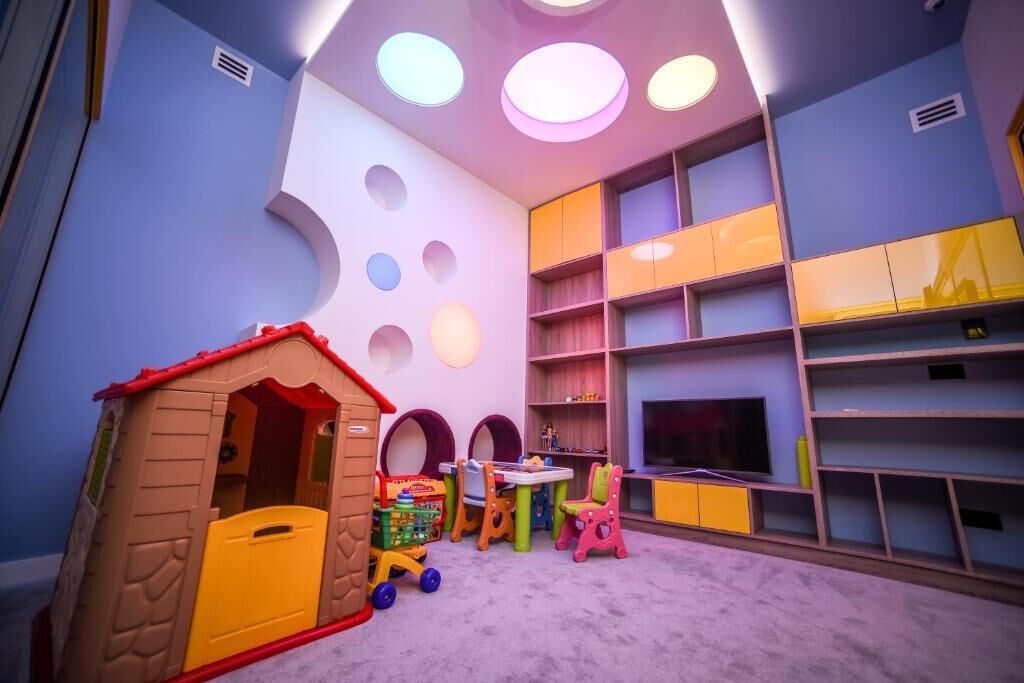 Zona infantil con una casita de juegos, una mesa, sillas y una televisión.