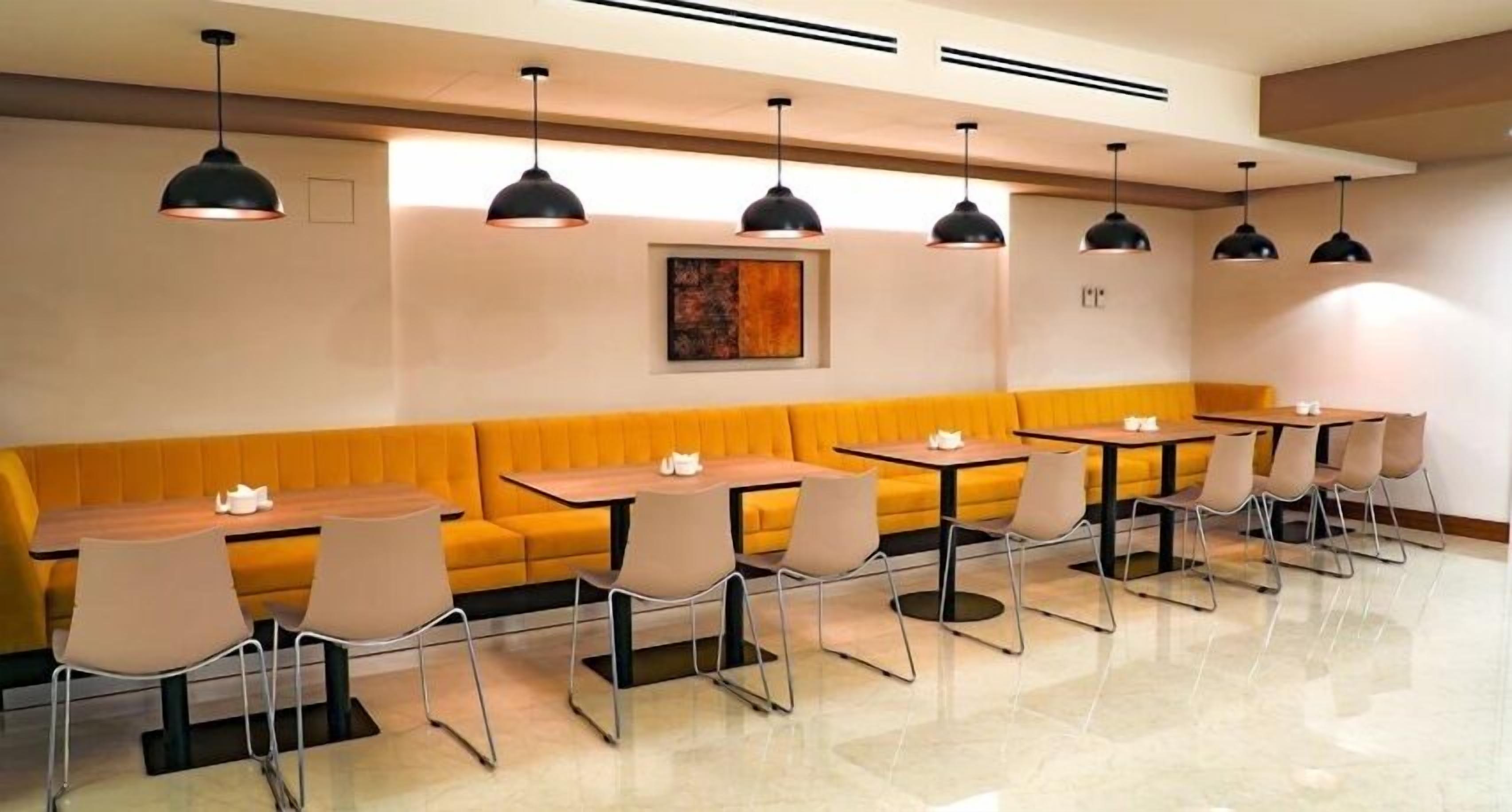 A modern restaurant with a yellow booth seating area, multiple tables, and pendant lighting.