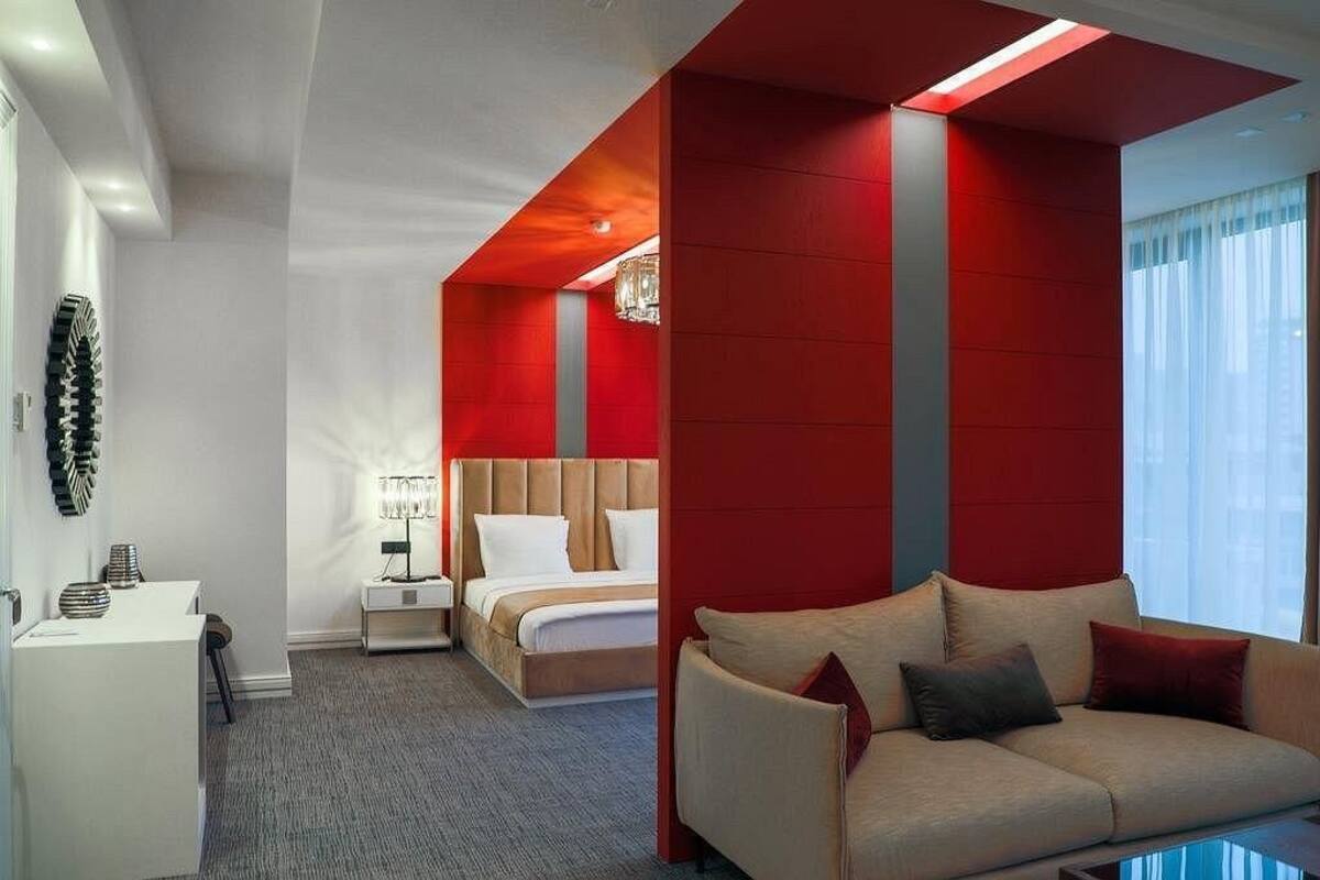 A hotel room with a bed, a desk, a sofa, and a large window.