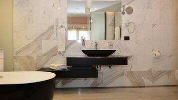 A modern bathroom with a marble wall, a black sink, a large mirror, and a black bathtub.