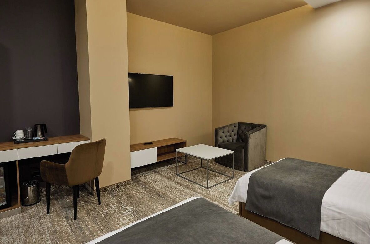 Quarto de hotel com escrivaninha, cadeira, duas camas, televisão e máquina de café.