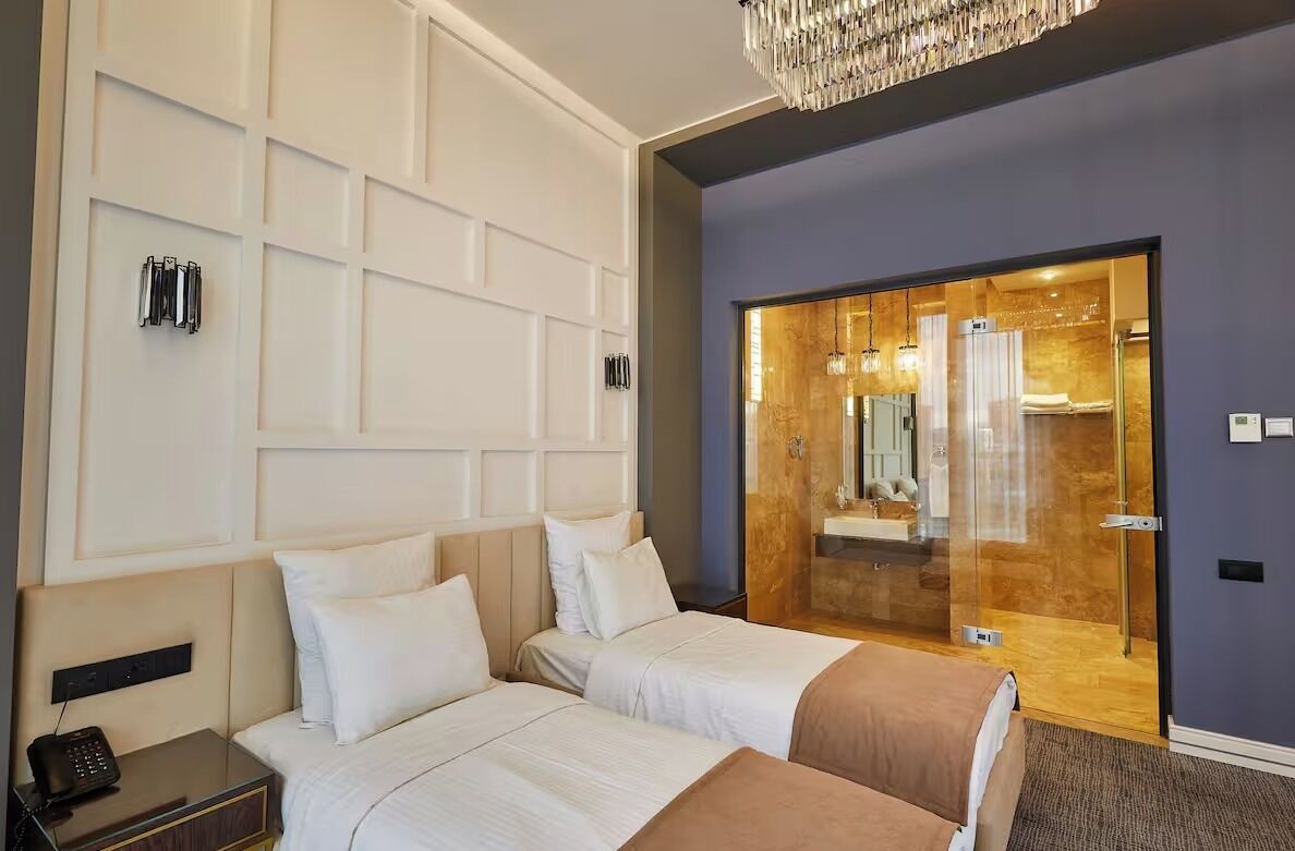 Quarto de hotel com duas camas, porta de madeira que dá para um banheiro e um candelabro.