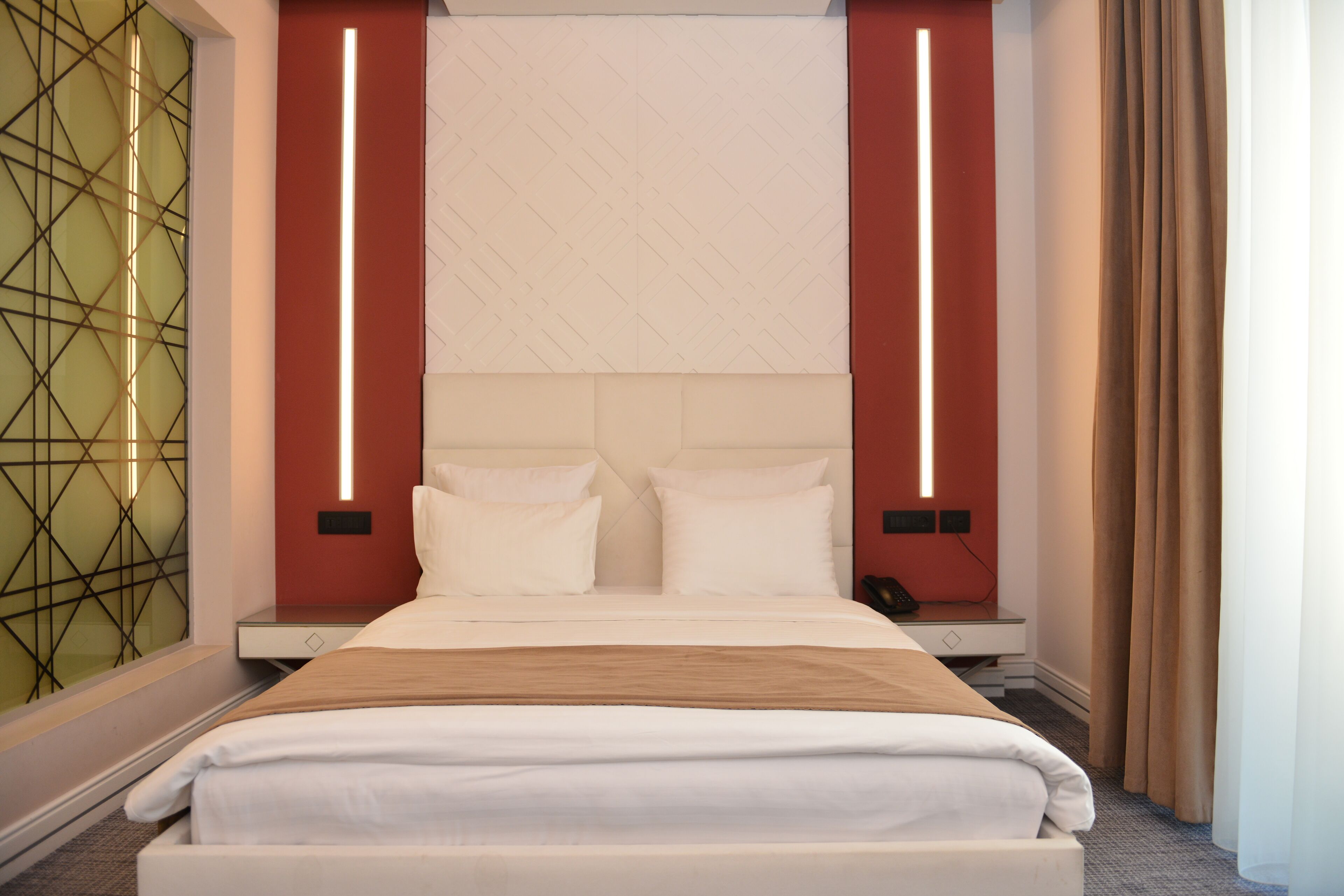Une chambre d’hôtel moderne dotée d’un grand lit, d’une tête de lit agrémentée de panneaux lumineux verticaux, d’une table de chevet et d’un panneau décoratif mural.