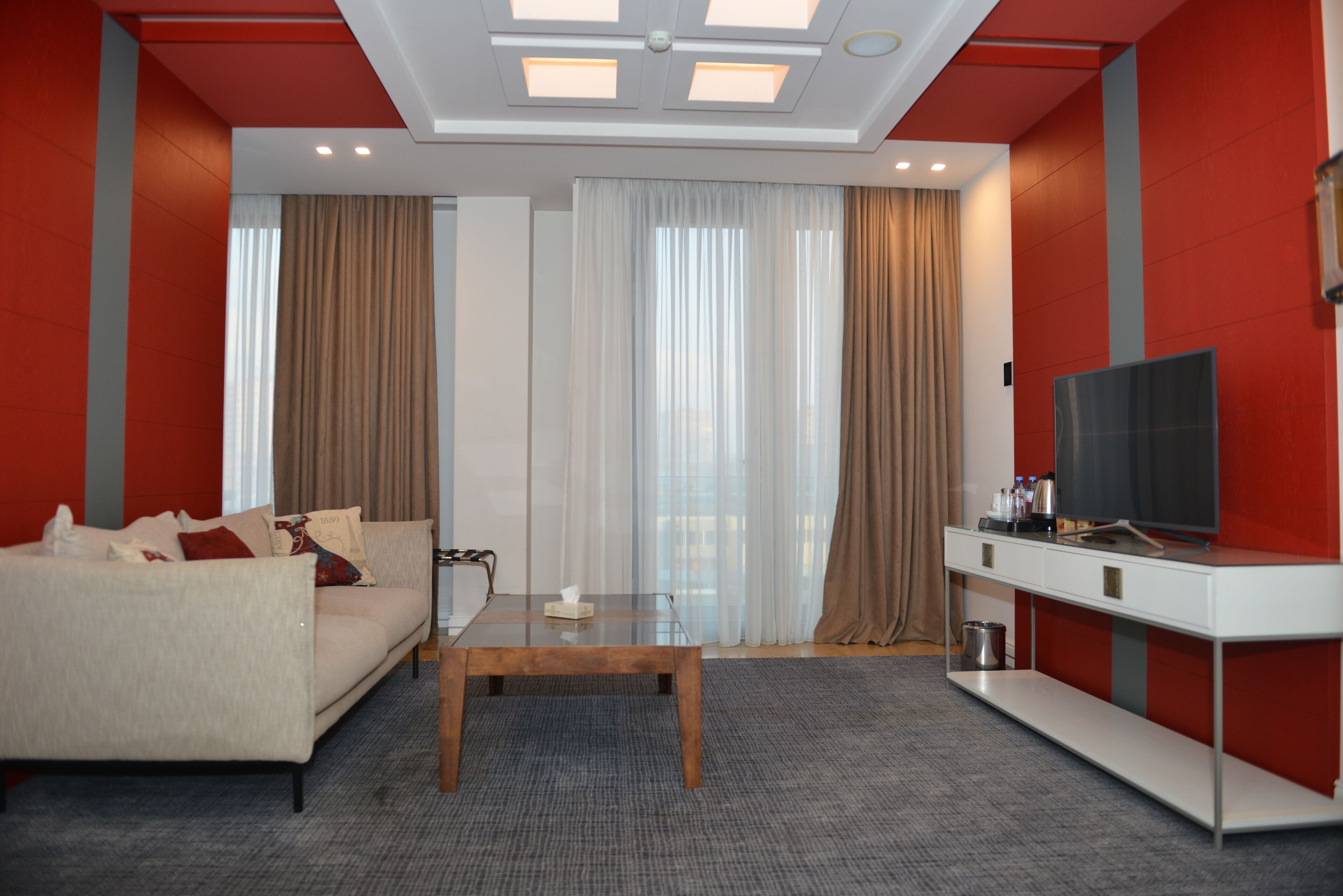 Een moderne hotelkamer met een bank, een bijzettafeltje, een televisie en gordijnen.