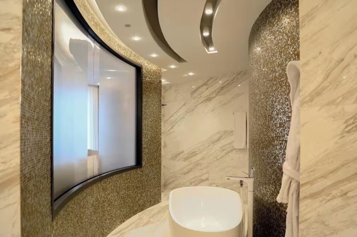A modern bathroom with a large mirror, a bathtub, and a marble wall.