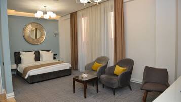Habitación de hotel con una cama, dos sillones con cojines amarillos, una mesita y un espejo grande en la pared.
