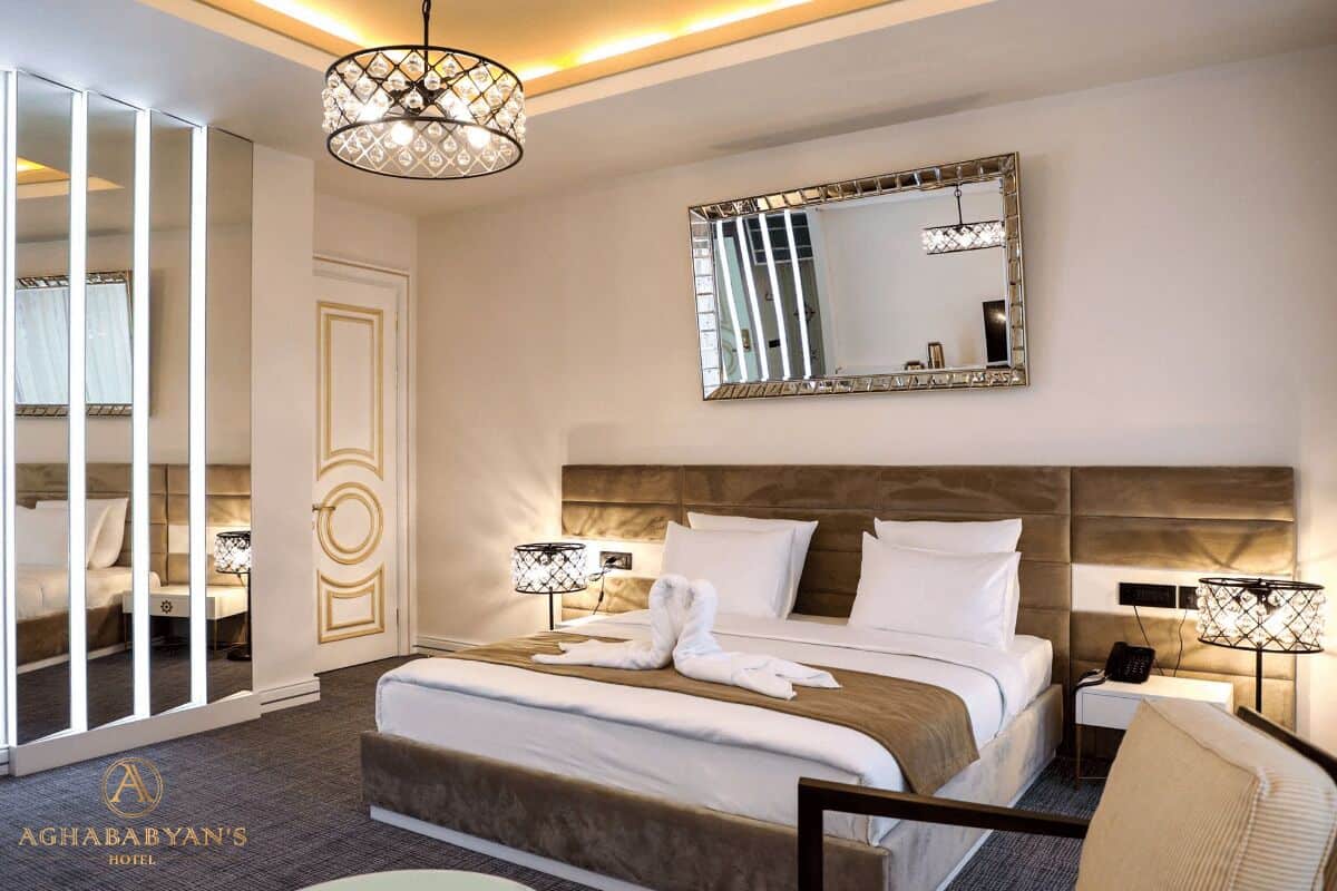 A hotel room with a large bed, a mirror, two bedside lamps, and a chandelier.