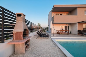 Ein Poolbereich mit Grill, Liegestühlen und einem modernen Gebäude.