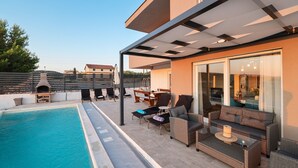 Eine Dachterrasse mit Pool, Sitzgelegenheiten im Freien und einem überdachten Essbereich.