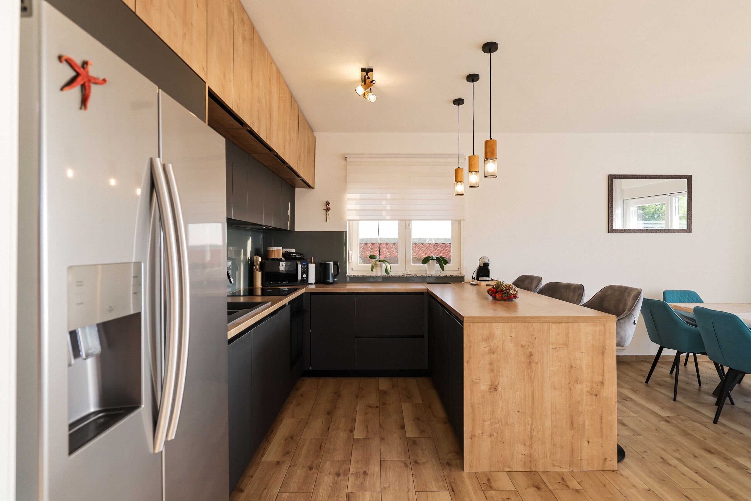 A modern kitchen with a central island, stainless steel appliances, wooden cabinetry, and a dining area with chairs.