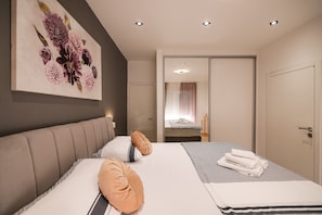 Ein modernes Hotelzimmer mit einem großen Bett, einer Kopfteil, einem Blumenbild und einem Badezimmer mit Spiegel sowie einer Tür.