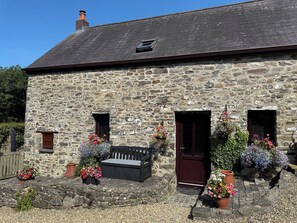 A stone building with a sloped roof, a wooden bench, and flower pots. - Old Farmhouse Cottage (Llandysul)
