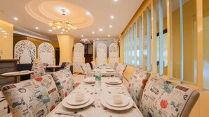 A dining area with a long table set for four, surrounded by patterned chairs, and a decorative ceiling light. - Hotel Triple Three By Aditya Inn (Jaipur)