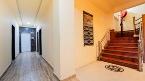 A hallway with a wooden floor, a staircase with a metal railing, and a door at the end. - Hotel Triple Three By Aditya Inn (Jaipur)