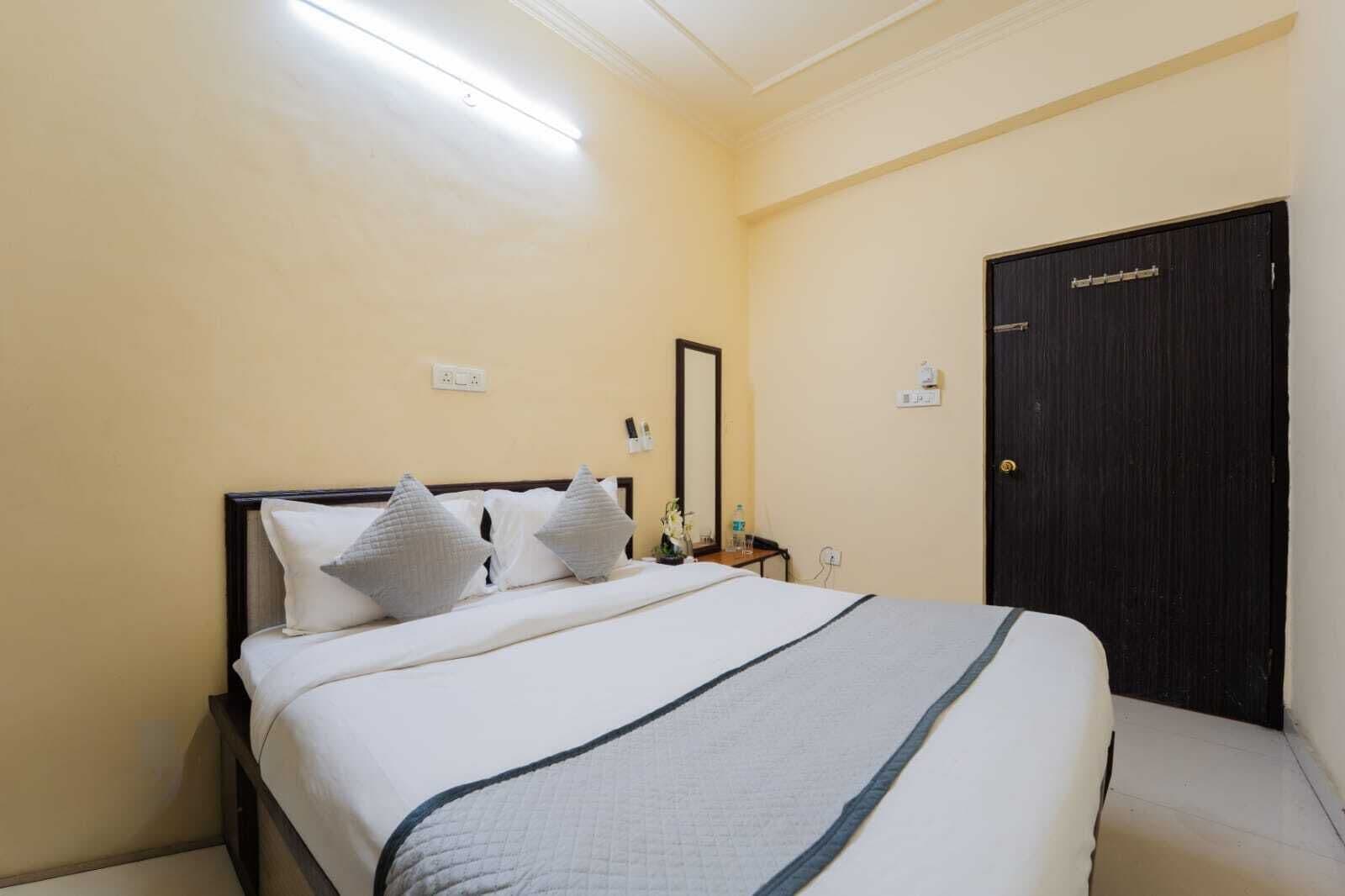 A hotel room with a bed, a nightstand, a mirror, a door, and a ceiling light.