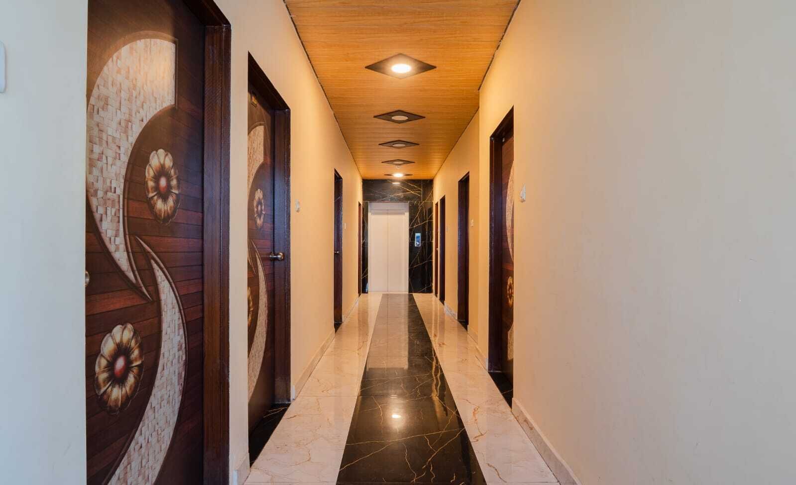 Un pasillo con suelo de mármol, puertas de madera y techo de madera con iluminación empotrada.
