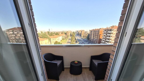 A balcony with two black chairs and a small round table, overlooking a cityscape with buildings and a road. - CHECK-INGANNI, above MM1 Inganni and next to the Italian Diagnostic Center (Milano)