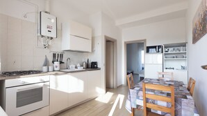 A modern kitchen with white cabinets, a built-in oven, and a gas stove. There is a dining area with a wooden table and chairs. - CHECK-INGANNI, above MM1 Inganni and next to the Italian Diagnostic Center (Milano)