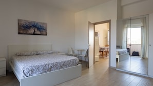 A modern bedroom with a large bed, a small table, and a chair. There is a painting on the wall and a mirror on the door. - CHECK-INGANNI, above MM1 Inganni and next to the Italian Diagnostic Center (Milano)