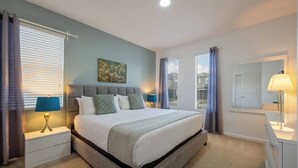 Un dormitorio con una cama grande, una mesita de noche con lámpara, un aparador y una ventana con cortinas.