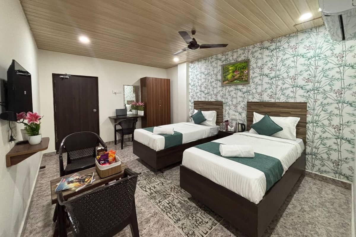 Quarto de hotel com duas camas, uma escrivaninha, uma cadeira, uma televisão e um ventilador de teto.