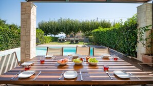 An outdoor dining area with a pool view, wooden table, and chairs.