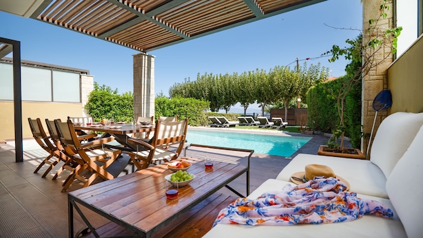 En udendørs terrasse med swimmingpool, træmøbler og en hvid sofa.