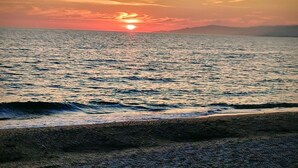 A sunset over a calm sea with a beach in the foreground.