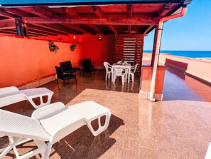A covered outdoor seating area with white chairs and tables, a red wall, and a view of the ocean. - Haus Filippa mit Entspannungsterrasse by Interhome (Balestrate)