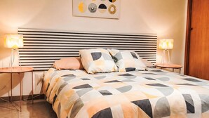 Quarto bem organizado com cama, mesas de cabeceira e uma obra de arte na parede.