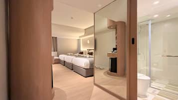 Quarto de hotel moderno com uma cama grande, área de estar, TV e chuveiro em gabinete de vidro.