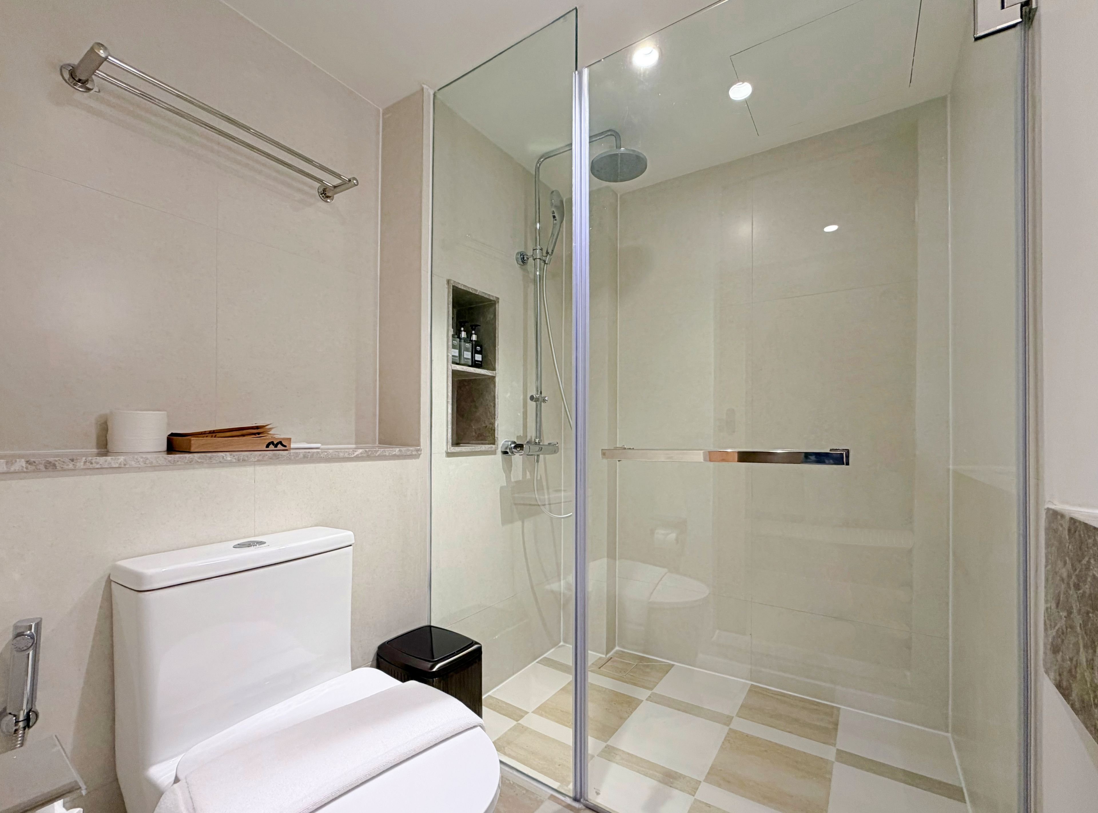 A modern bathroom with a glass-enclosed shower, a toilet, and a shelf with toiletries.