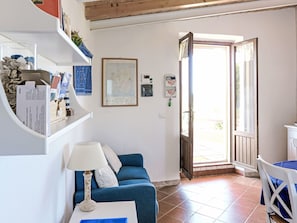 Un salon avec un canapé bleu, une table blanche sur laquelle se trouve une lampe, une carte accrochée au mur et une porte donnant sur l’extérieur.