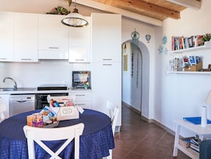 Une cuisine moderne avec des meubles blancs, un four encastré et un coin repas agrémenté d’une nappe bleue.