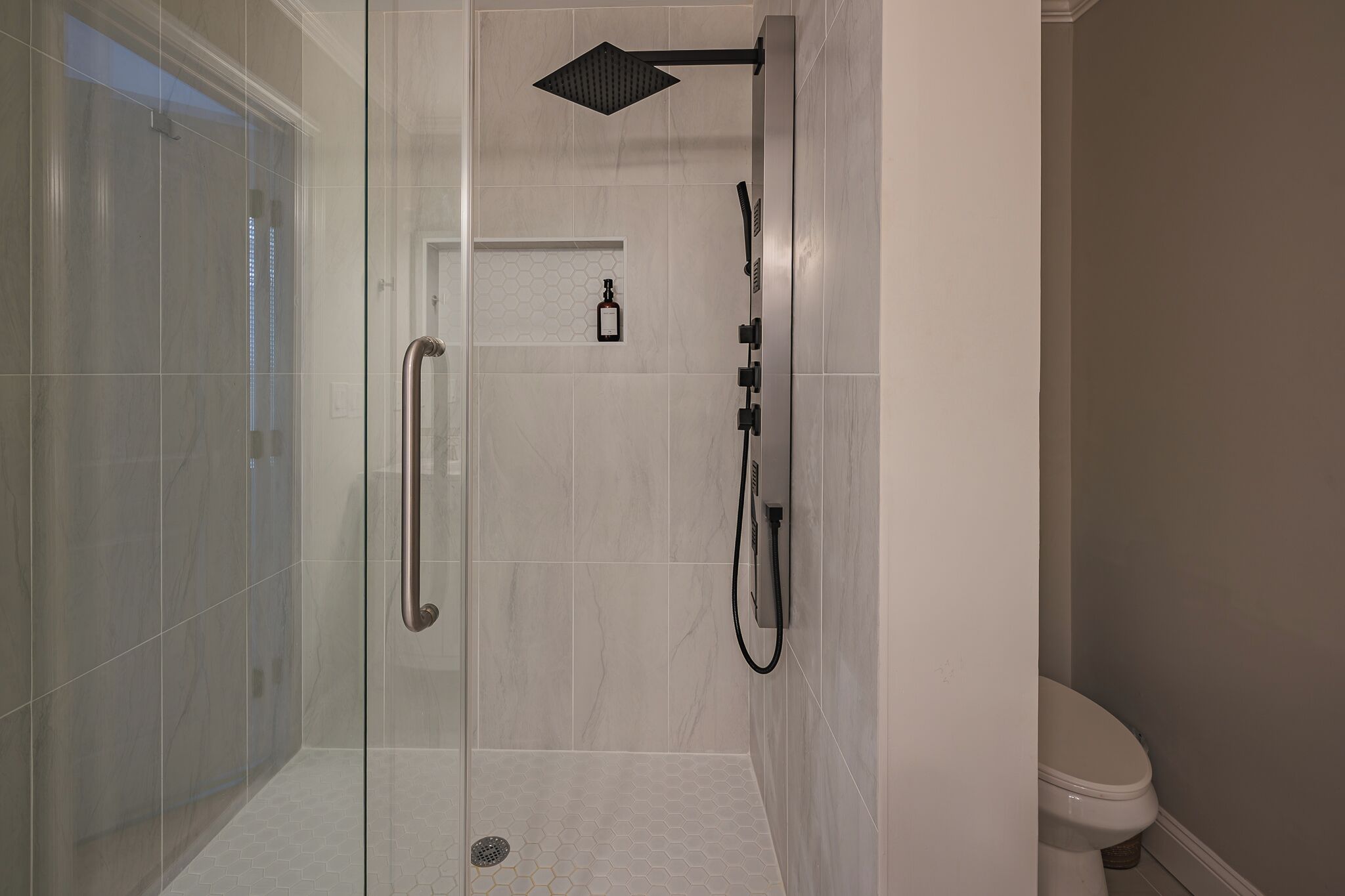 Een moderne badkamer met een douchecabine van glas, een wit toilet en een klein plankje met een fles.