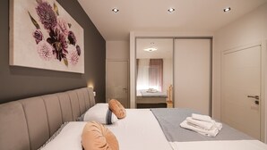 A modern hotel room with a large bed, a headboard, a painting of flowers, a bathroom with a mirror, and a door. - Villa Carmen Zadarvillas (Sukosan)