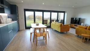 A modern kitchen with a dining area, a sofa set, and a TV. - Glynllifon 6 (Marianglas)