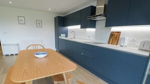 A modern kitchen with dark blue cabinets, a wooden dining table, and a white countertop. - Glynllifon 6 (Marianglas)