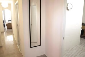 A hallway with a mirror, a clock, and a door leading to another room.
